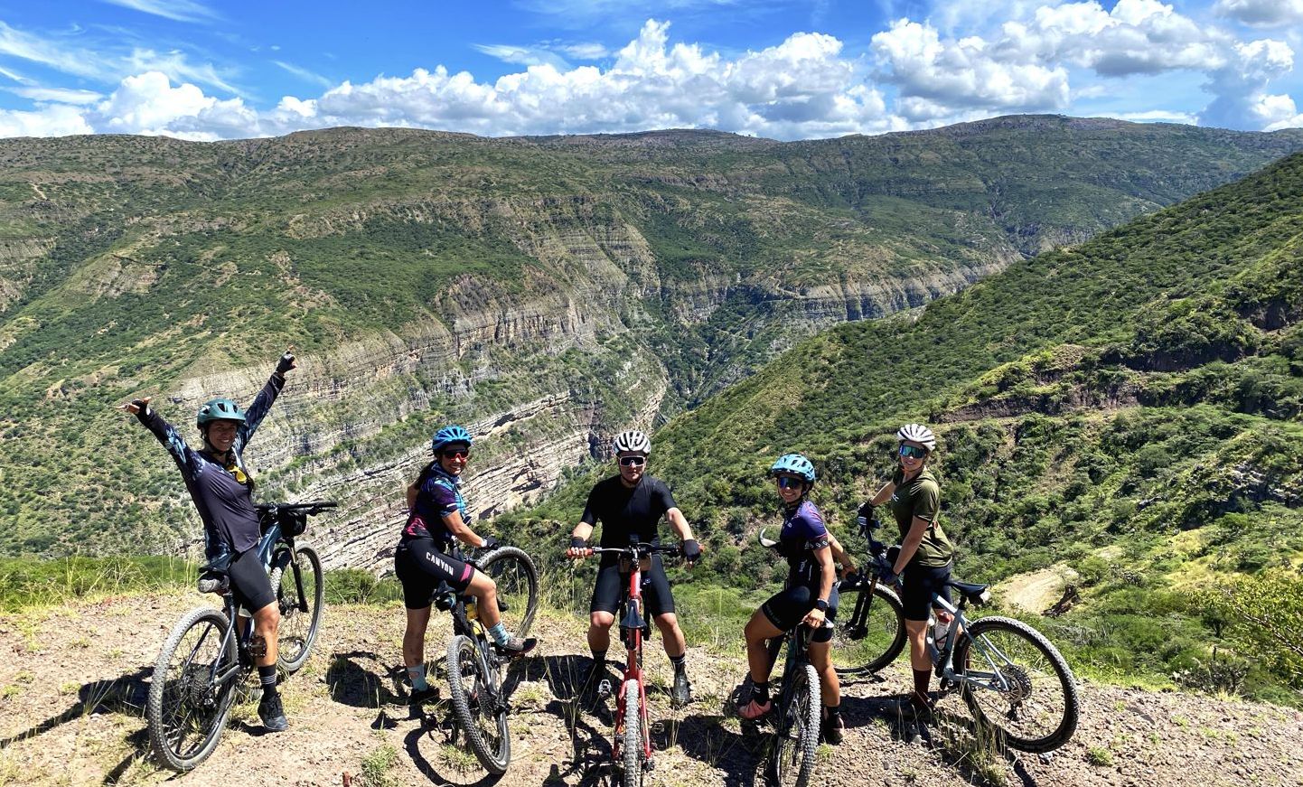 A group of riders cheering with their bikes on a canyon-rim road