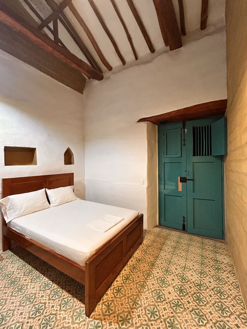 A whitewashed hotel room with a wooden door and patterned tile floor