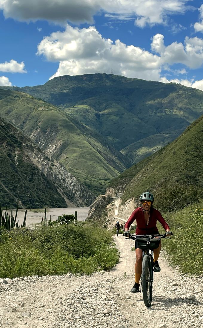 A rider descending a gravel road between green mountains